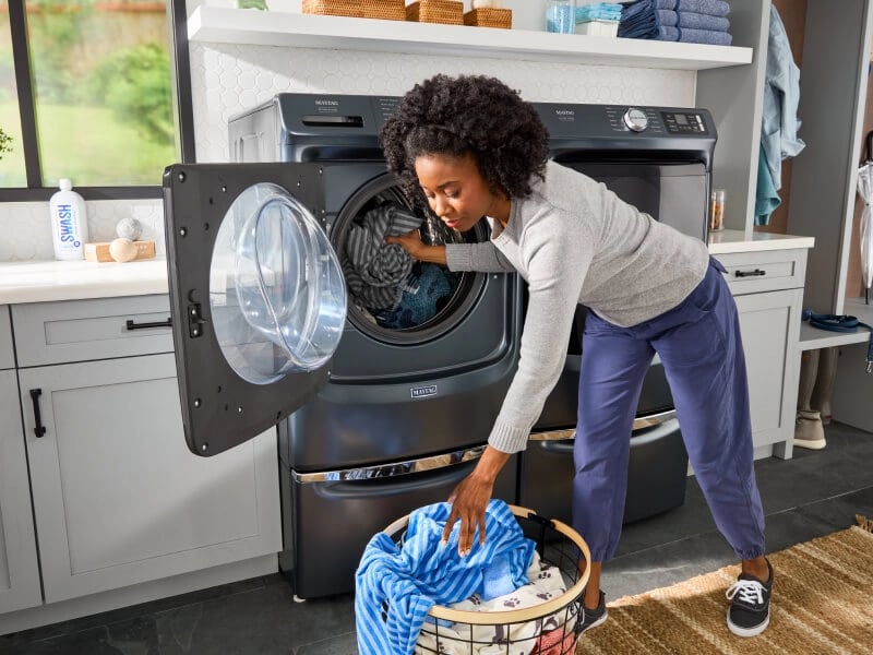 A woman putting laundry in her Maytag® washing machine