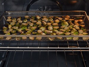 Air fryer basket with Brussels sprouts inside an oven
