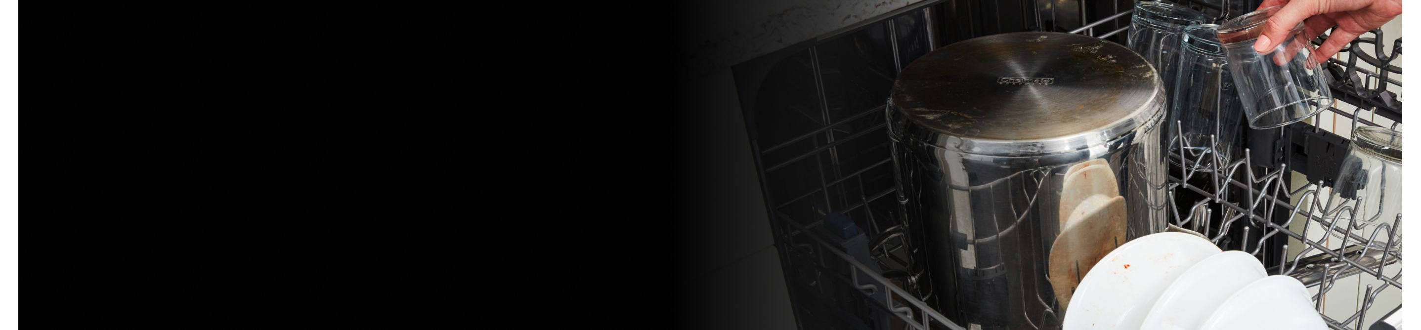 A metal stock pot and other dirty dishes loaded in a dishwasher rack