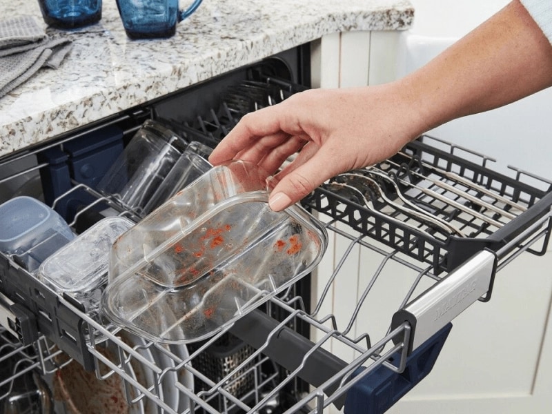 Person loading dishwasher with a dirty plastic container