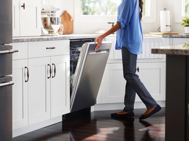 Person closing a stainless steel dishwasher