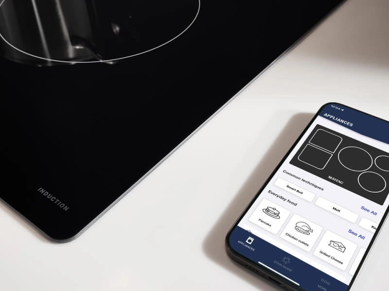 Phone with Maytag® App on counter next to cooktop