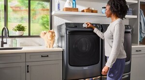A person engaging with their washer in the laundry room with their cat next to them