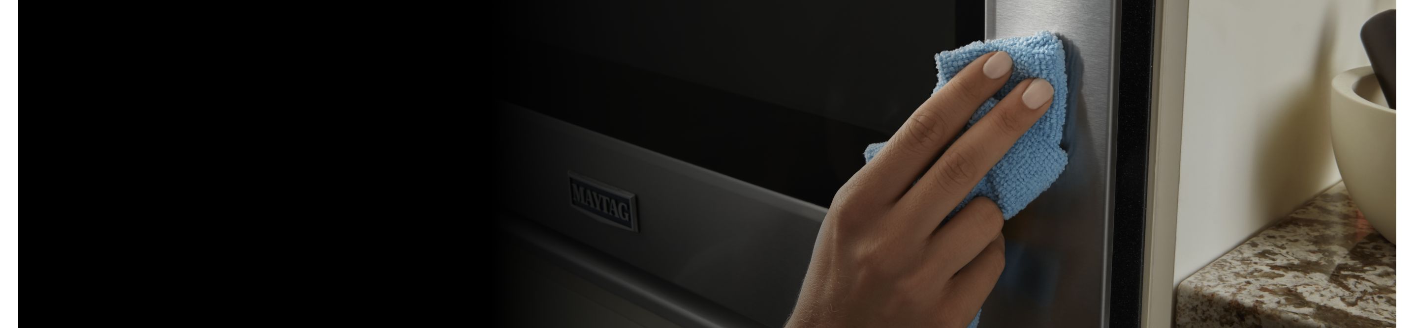 A hand holding a cloth wiping down the exterior of the oven door 