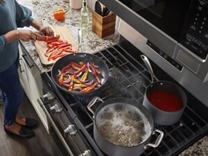 Person cutting peppers next to food cooking on a gas stovetop
