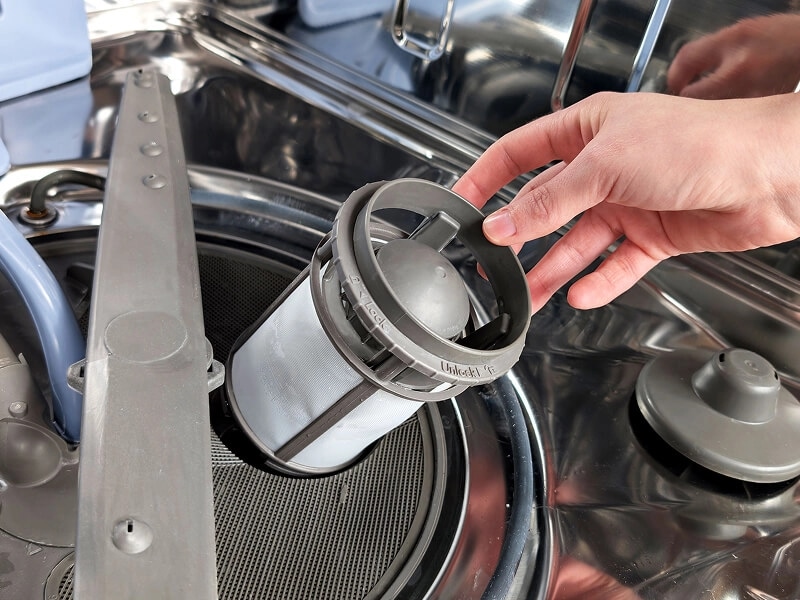 A hand removing the filter on a dishwasher