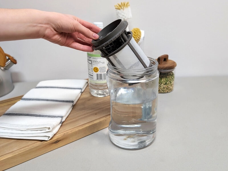 A person pulling a dishwasher filter from a glass of vinegar