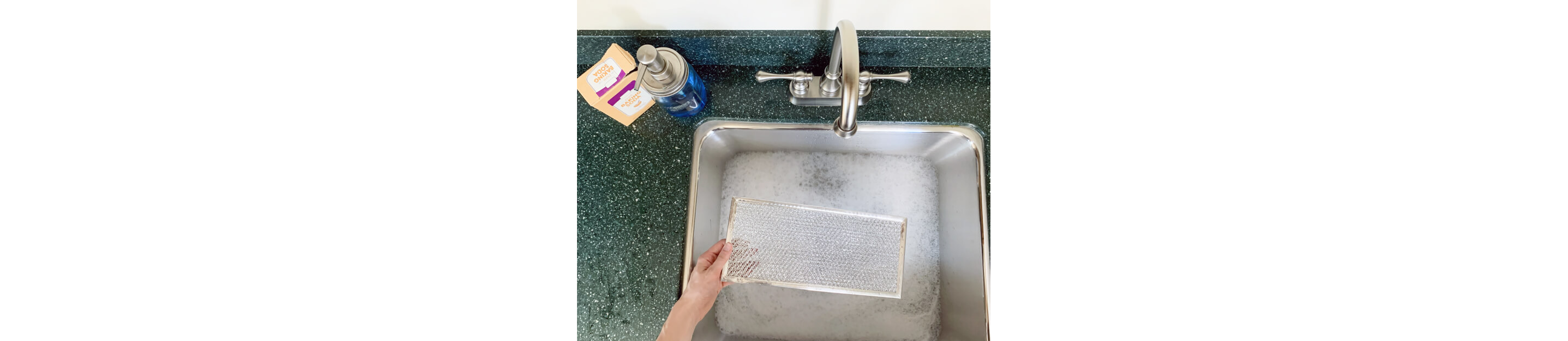 Hand lowering grease filter into sink with soapy water