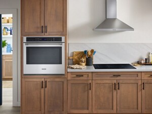A kitchen with a stainless wall oven, brown cabinetry and a glass cooktop