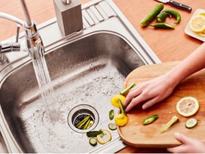A person sweeping vegetable pieces off a cutting board into the garbage disposal