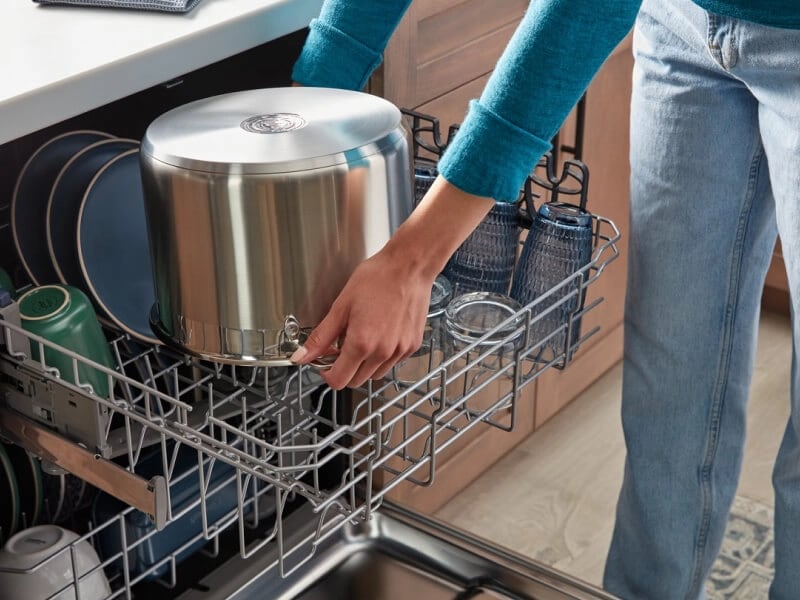 Woman loading a stainless steel pot into a dishwasher