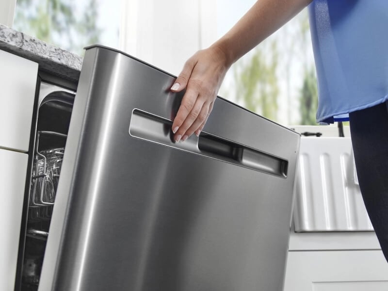 Woman closing a dishwasher in bright kitchen