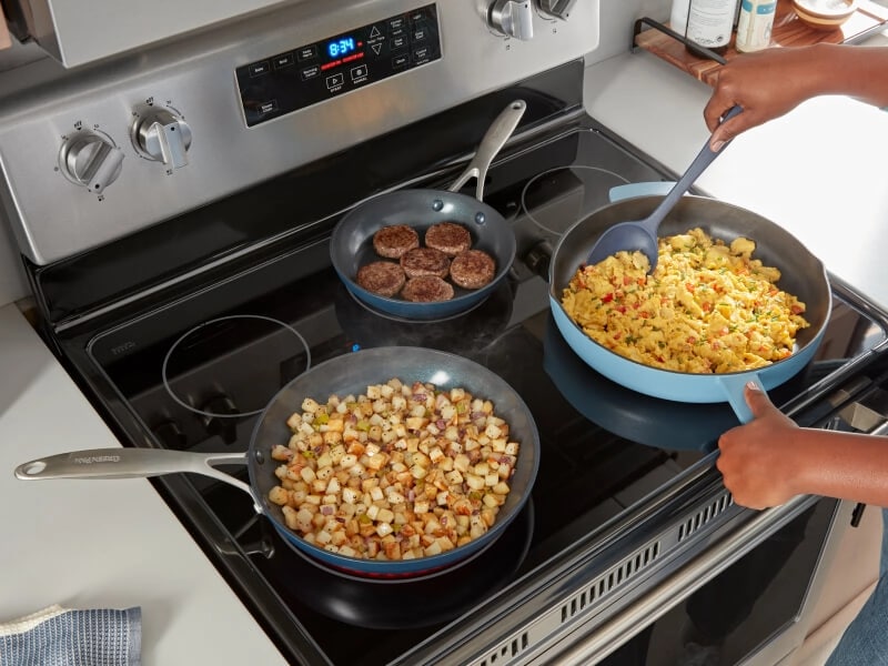 A woman stirring pasta in a pan with two more dishes on the stove