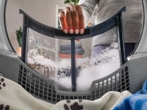 Hand pulling a lint trap out of a dryer with a dog blanket inside