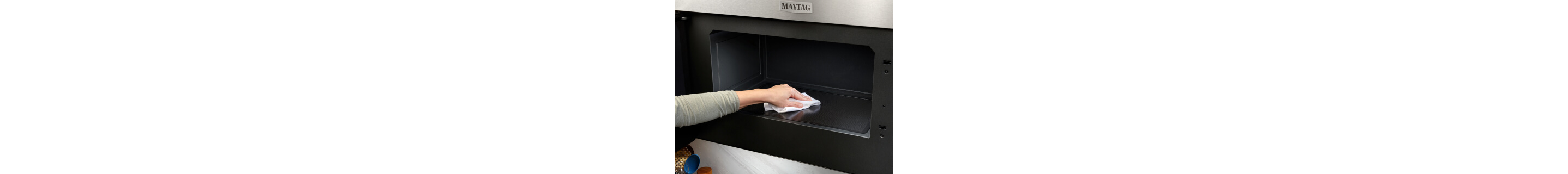 Person wiping down the interior of a Maytag® microwave