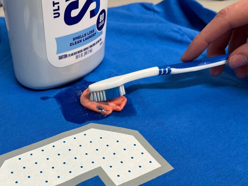 Person cleaning a gum stain with detergent and a toothbrush