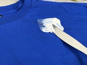 Paint on a blue shirt with a small butter knife removing the excess