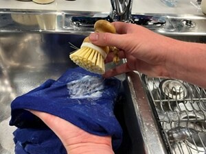Person scrubbing a blue shirt with a small brush