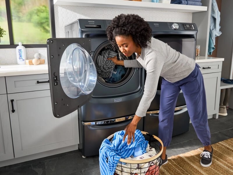 A woman loading clothes into a front load Maytag® washer