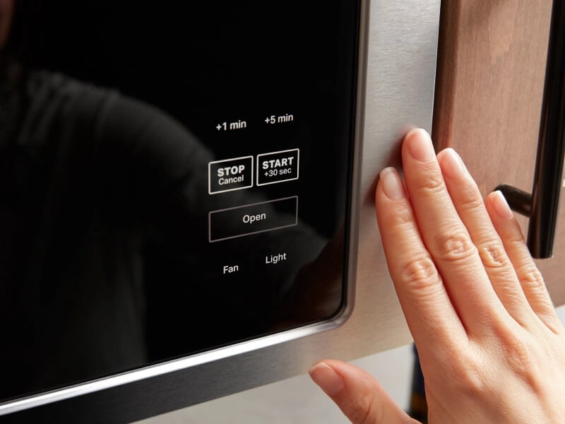 Fingers next to a built-in microwave control panel