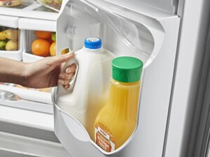 A person taking milk out of the door of a French door fridge
