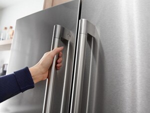 A hand shown pulling open a refrigerator door