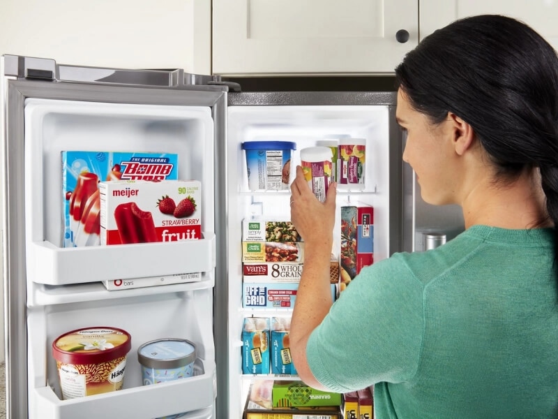 A woman storing a container of fruit in a side-by-side refrigerator door
