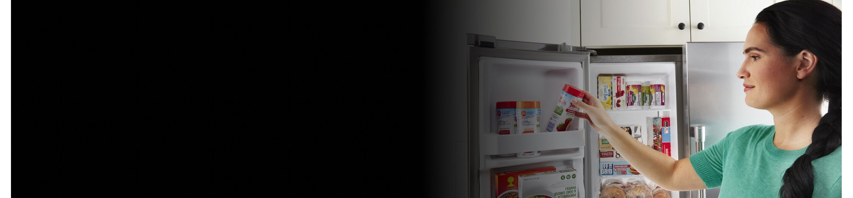 A person storing a container of fruit in a side-by-side refrigerator door