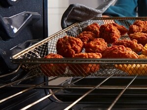 Hand pulling fried chicken and fries out of oven