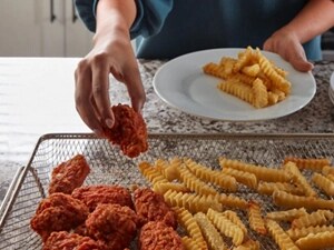 Hands holding a plate with fries on it in front of an air fry basket containing chicken pieces and fries