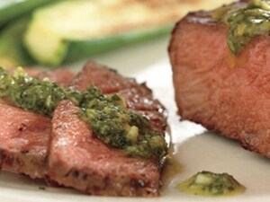 A close-up of slices of steak with a green sauce poured over them