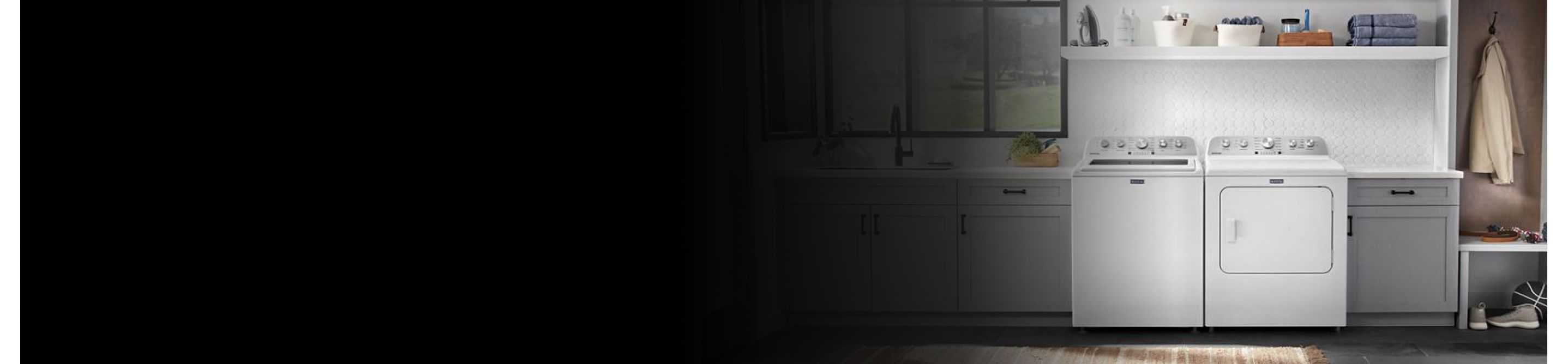 Overview of a laundry room with a top load washer, front load dryer, gray cabinets, and white backsplash tile.