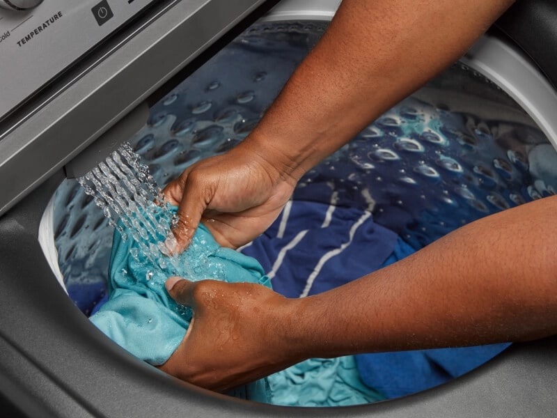 Person rinsing off an article of clothing underneath the built-in water faucet inside their washing machine