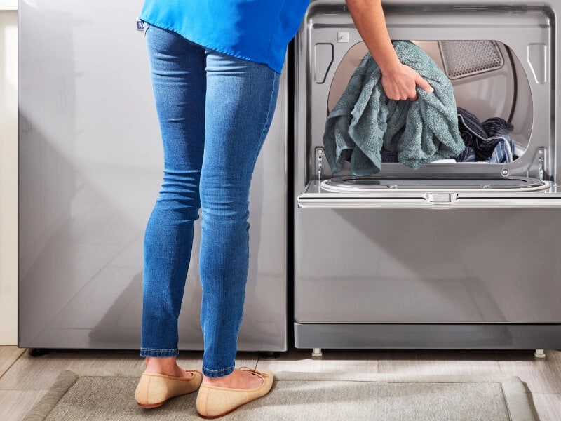 Person placing a teal towel inside of a white dryer