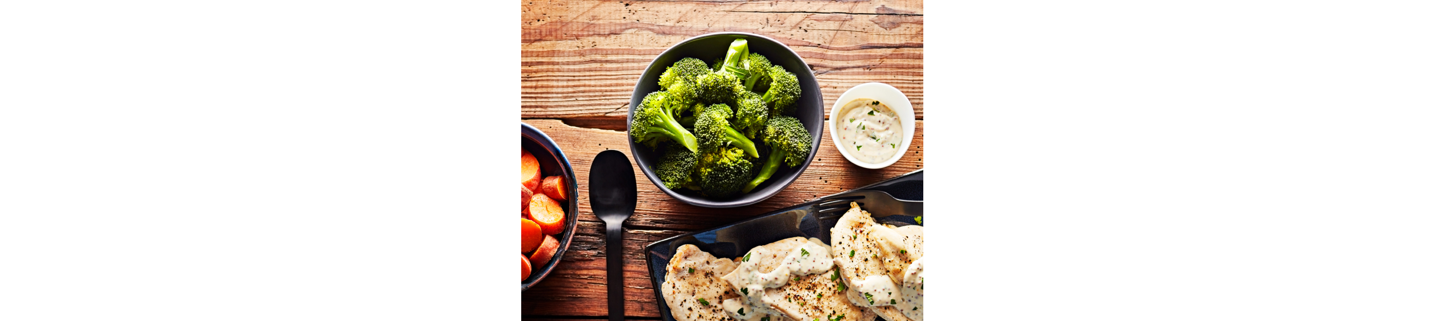 A close up of a bowl of steamed broccoli with a plate of grilled chicken breast and bowl of steamed carrots