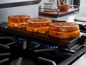 Three sandwiches cooking on a stovetop griddle