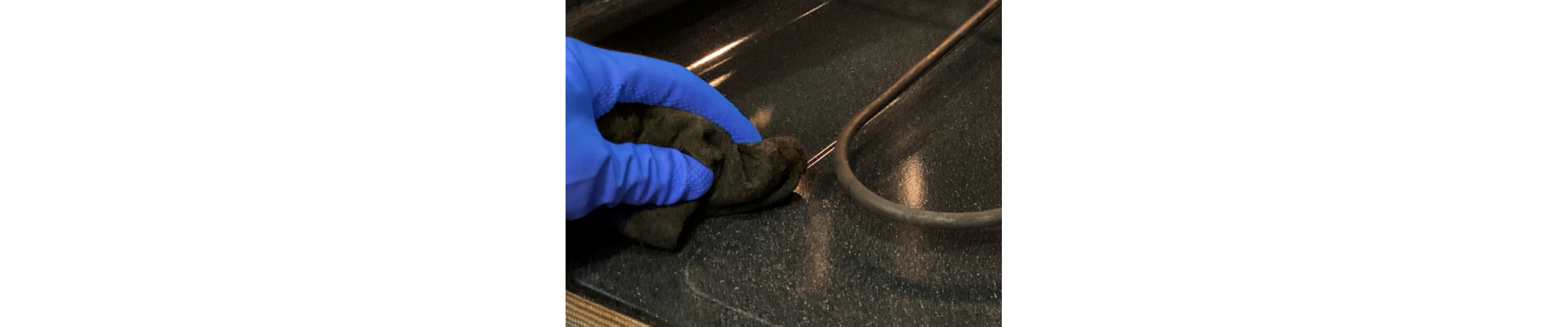 Close-up of hand in blue glove wiping around heat coils in oven cavity