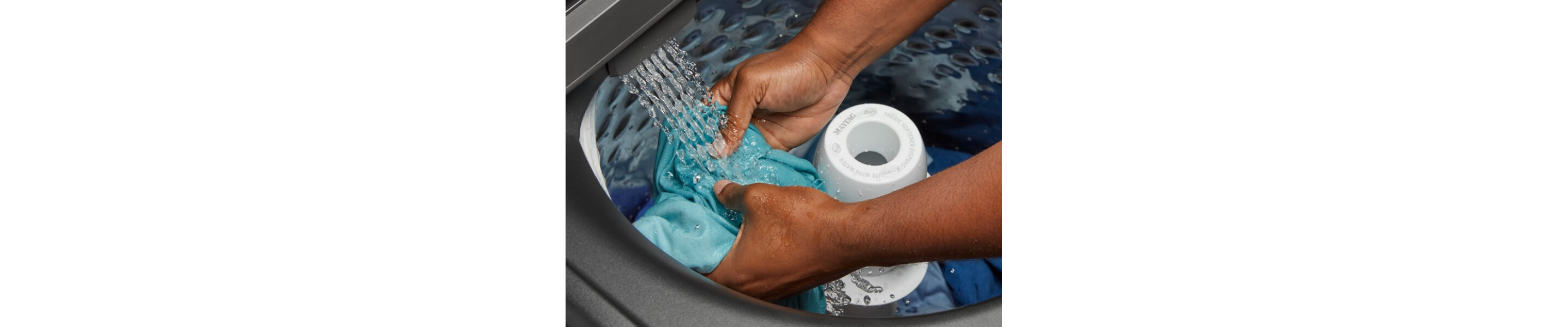 A person adding laundry to a Maytag® top load washing machine filling with water