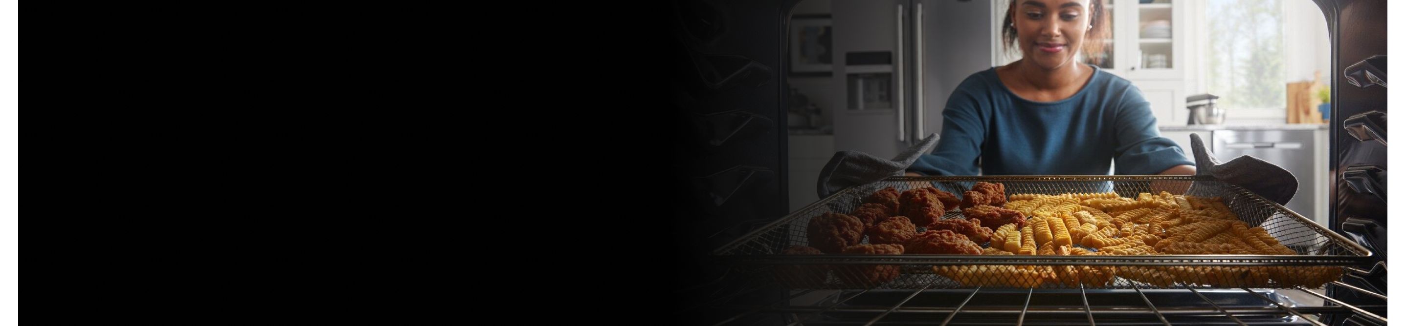 Person removing chicken strips and french fries from an oven