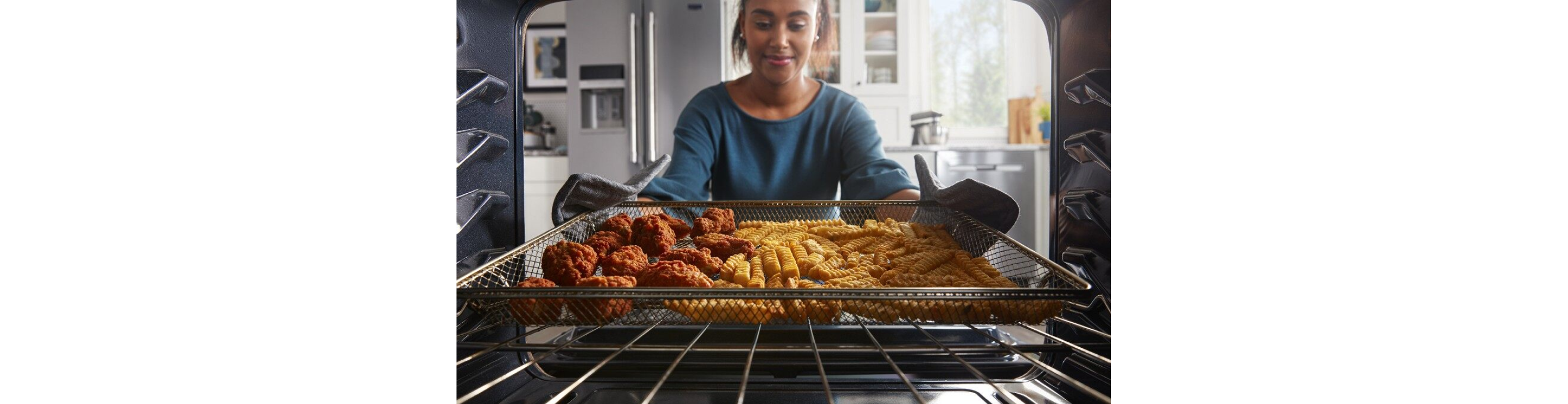 Person removing chicken strips and french fries from an oven