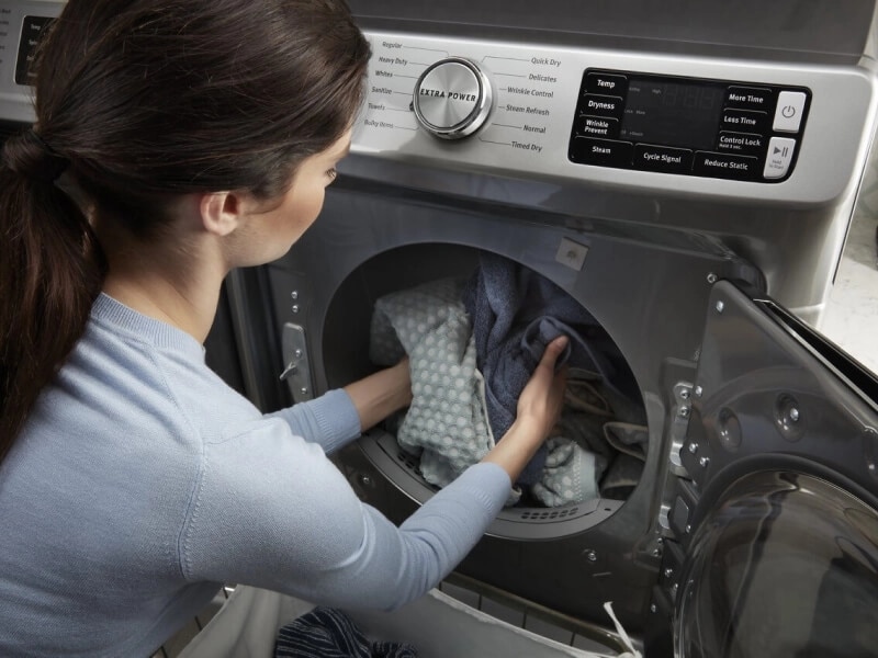 Person squatting down to pull laundry out of a Maytag® dryer with an Extra Power Button