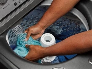 Hands holding a turquoise garment under water spray in a top load washer
