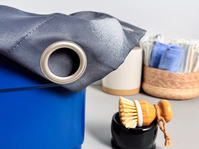 A blue curtain with a rung in a bucket next to a small scrub brush