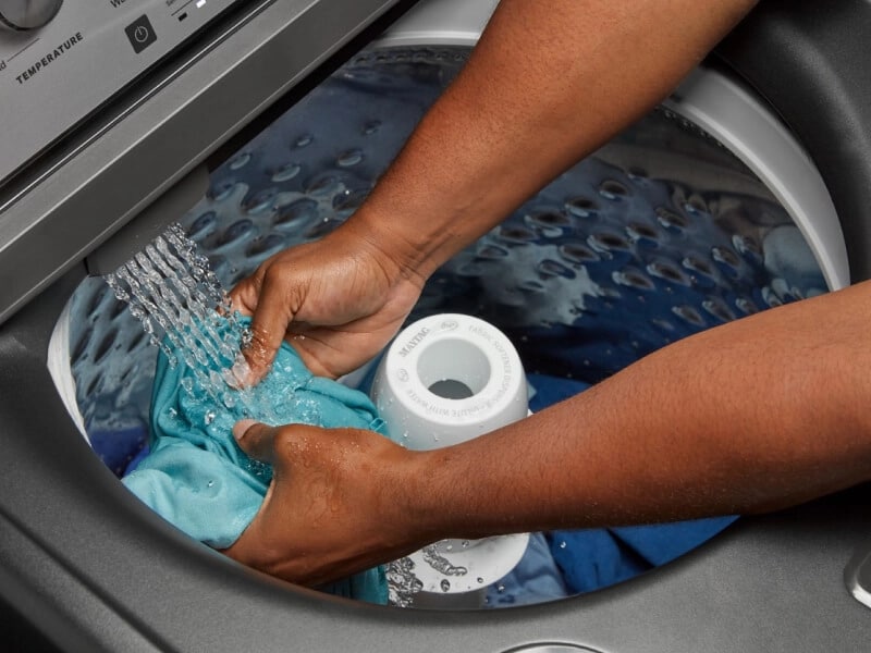 Someone holding a shirt in the washer as the water flows in