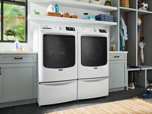 A white, front load washer and dryer pair in a laundry area with grey cabinets