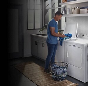 A man loading clothes into his white, top-load washer