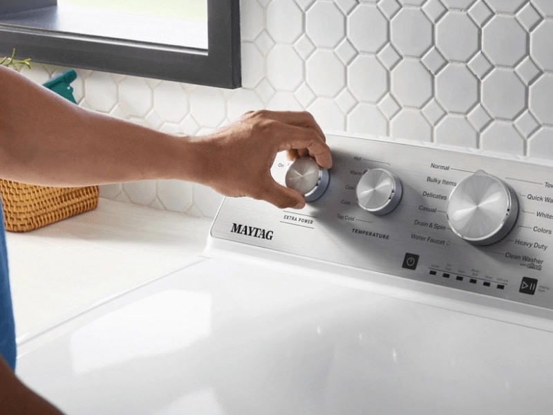 A hand turning a Maytag® washer dial to the Extra Power setting