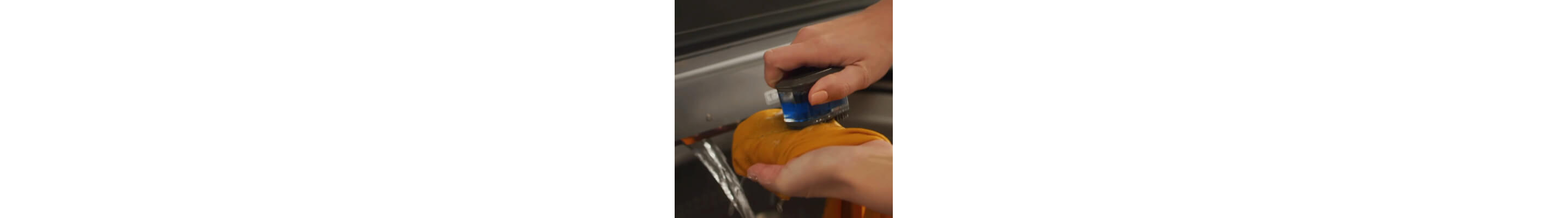 Person using scrub brush to pretreat stains under built-in water faucet in washer