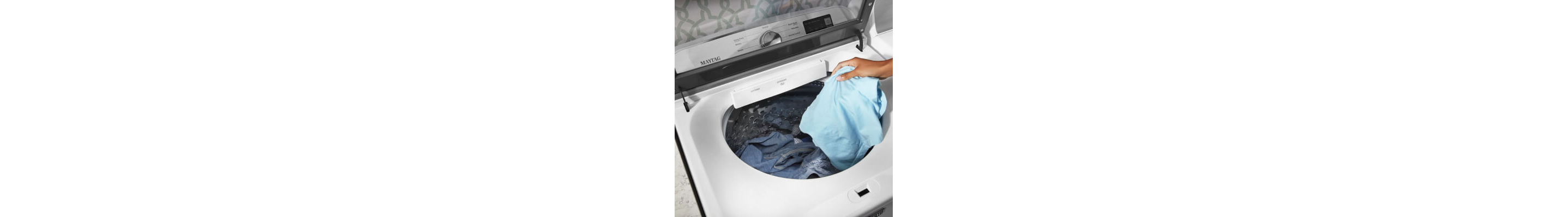 Person adding a blue garment to a white, top-load Maytag® washer