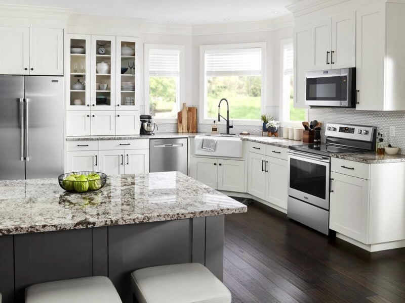 A kitchen with white cabinets, stainless steel appliances and counter seating